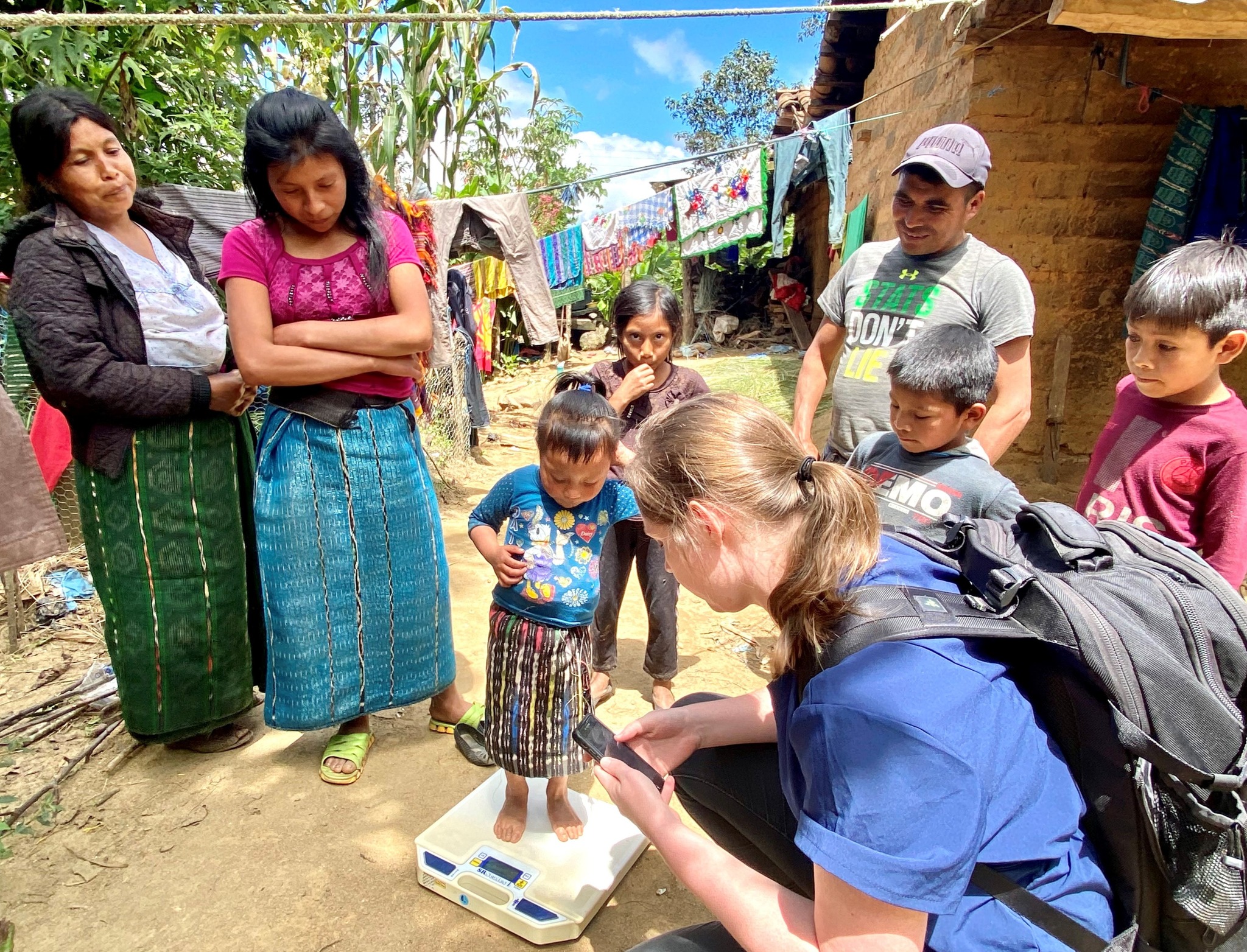 Missionary weighs a child in a village while family and friends watch