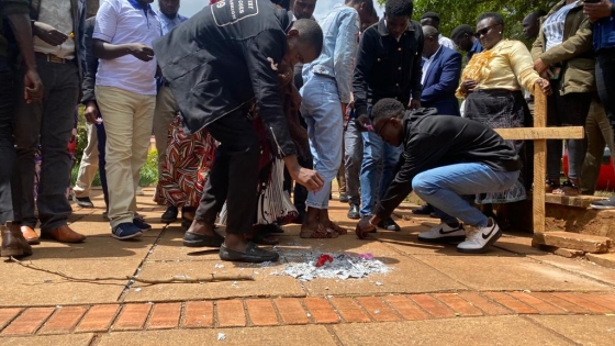 A group of people stand around a small wooden cross and burn notes where they have written their pain