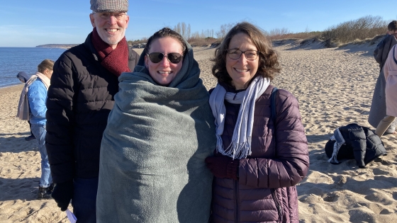 Resonate missionaries Steve and Chris Van Zanen stand on either side of Charlotte, who is wearing sunglasses and wrapped in a blanket, after her baptism in the Baltic Sea.