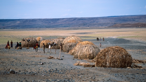 Vast rocky land with thatched huts and people standing nearby