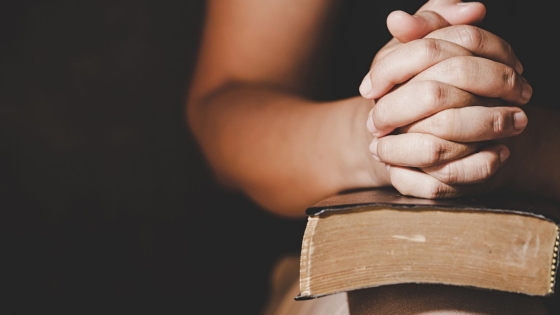 Hands folded in prayer on a Bible