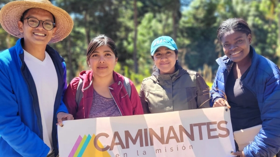 A group of young adults part of Cohort Central America stand with a "Caminantes" sign