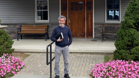 Gilbert Varela stands in front of a church building while holding a Bible