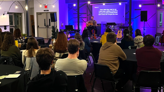 Young adults gathered at tables led in worship by a man playing a guitar