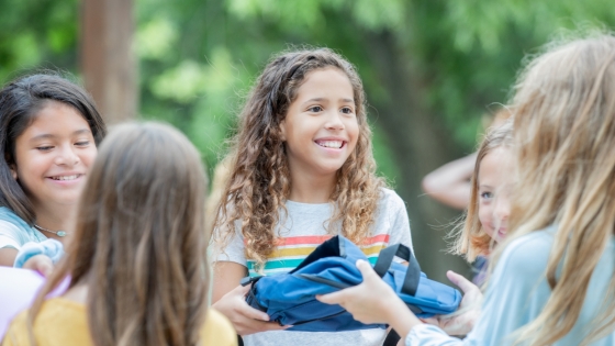 A smiling girl hands a bag to another girl