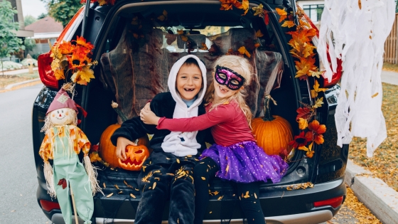 Two kids dressed in Halloween costumes sit in the trunk of a decorated car