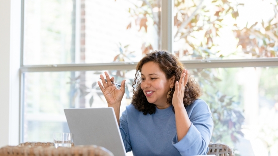 A woman smiles and holds her hands up while on a video call