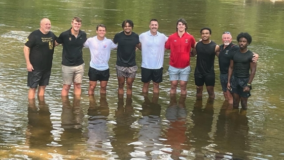 Coach Sam, Campus Minister Mike Wissink, and football players stand in the Muskegon River after getting baptized