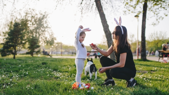 Woman, child, and dog gathering Easter eggs in a park