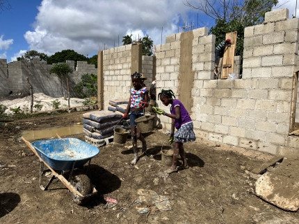 Two girls carry buckets to help with the construction of a church building