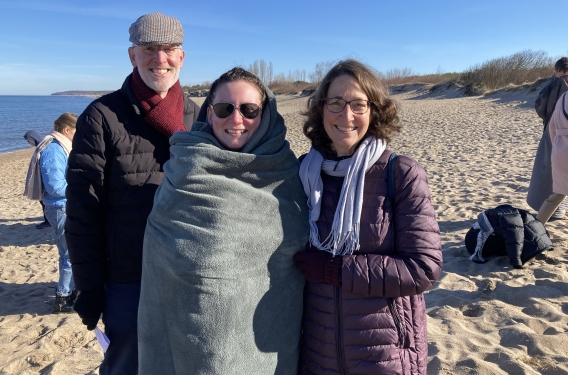 Resonate missionaries Steve and Chris Van Zanen stand on either side of Charlotte, who is wearing sunglasses and wrapped in a blanket, after her baptism in the Baltic Sea.
